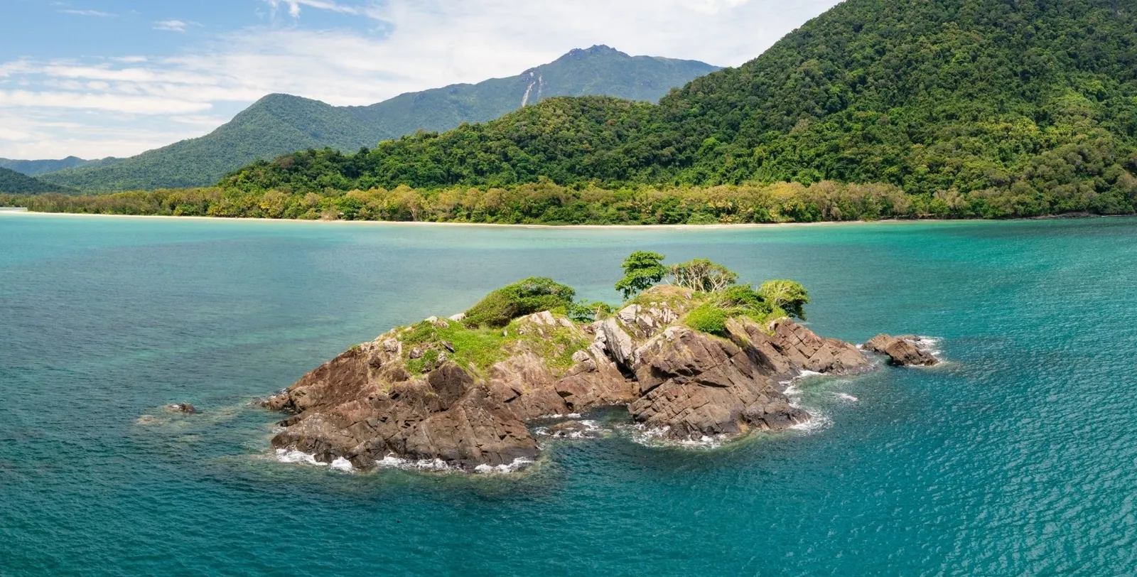 Rocky islet ringed by turquoise water off the Daintree coast, with rainforest-covered ranges behind