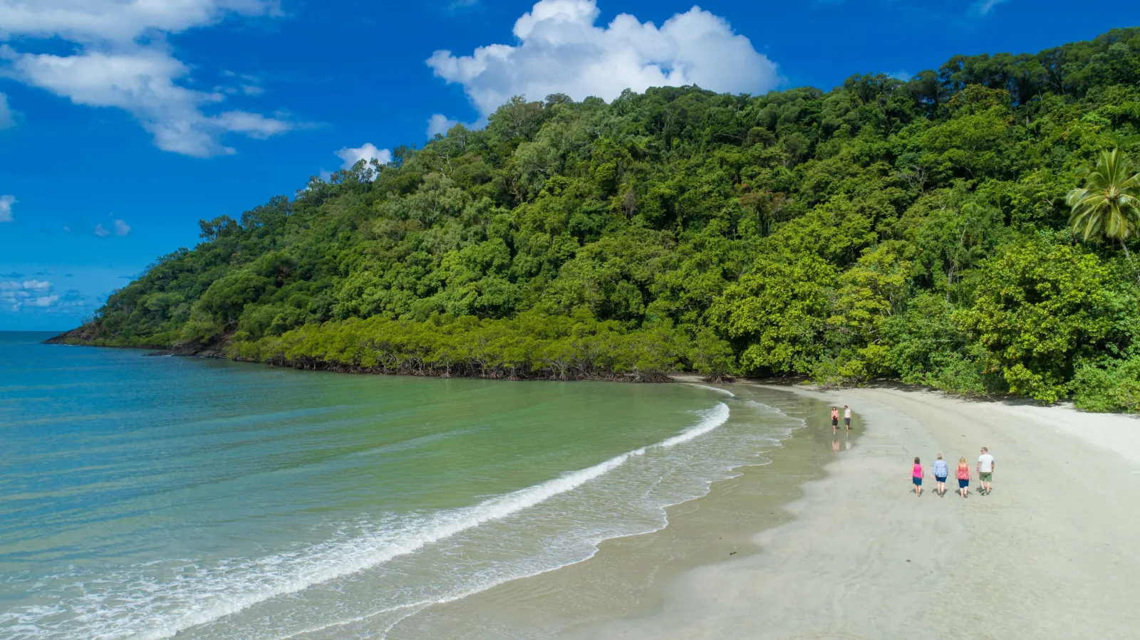 Visitors walking the beach at Cape Tribulation below rainforest-covered hills
