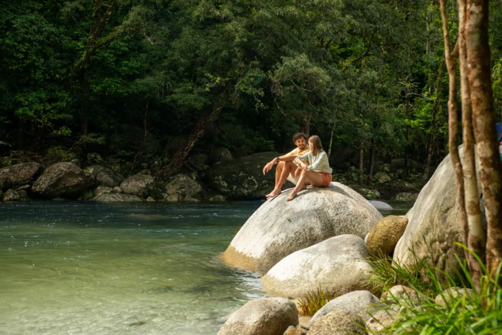 Visitors on a granite boulder beside a clear pool at Mossman Gorge