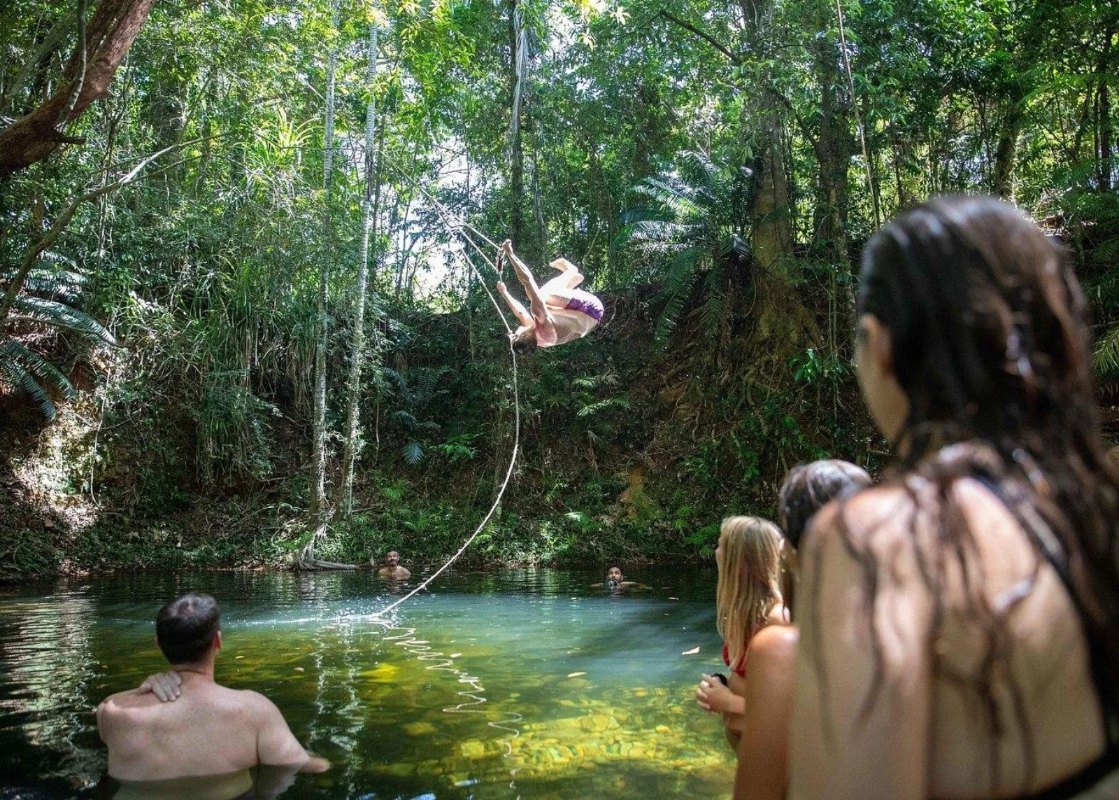 Swinger dropping into a rainforest waterhole as friends watch