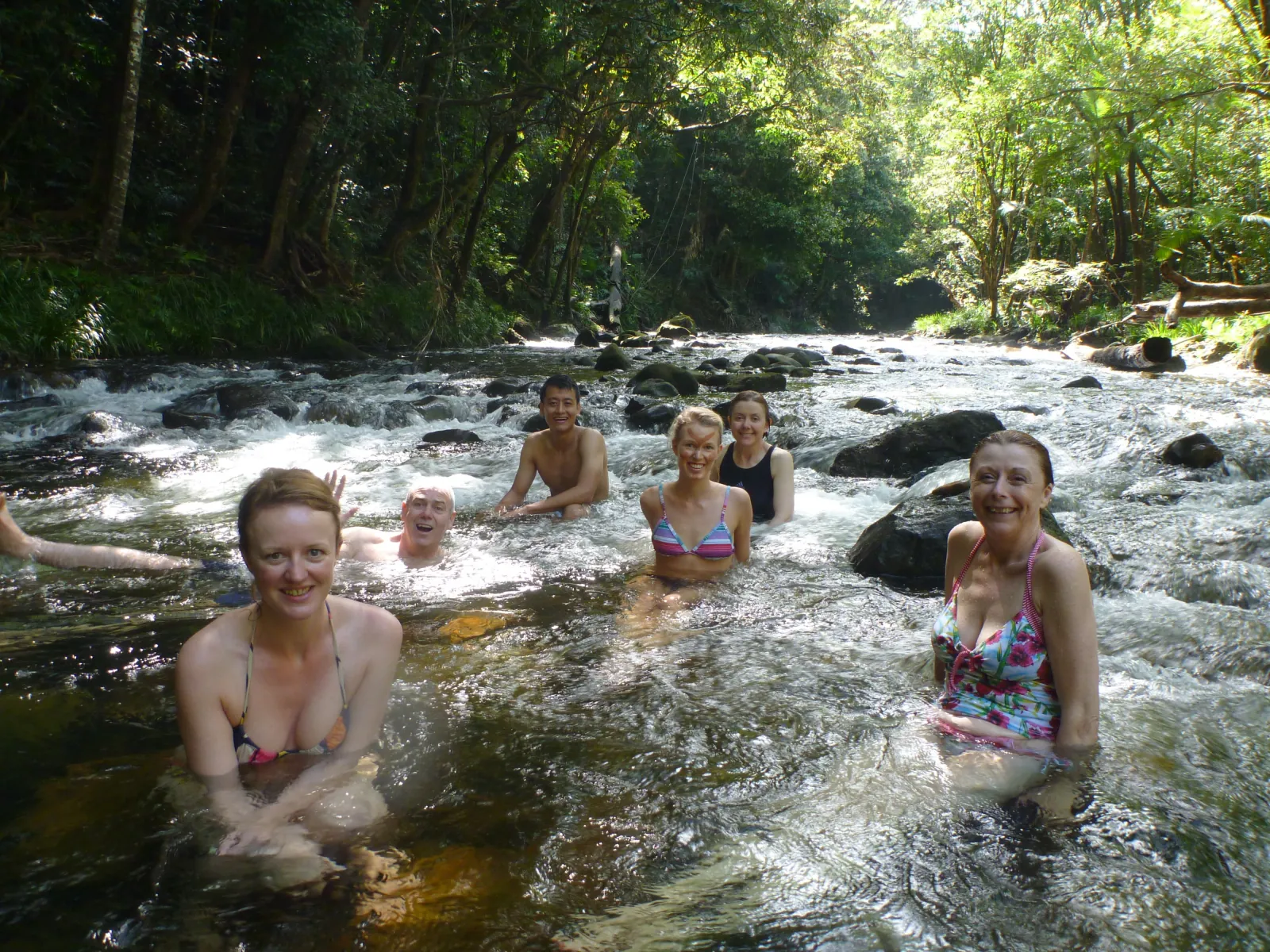 Guests swimming in a shallow rocky rainforest creek