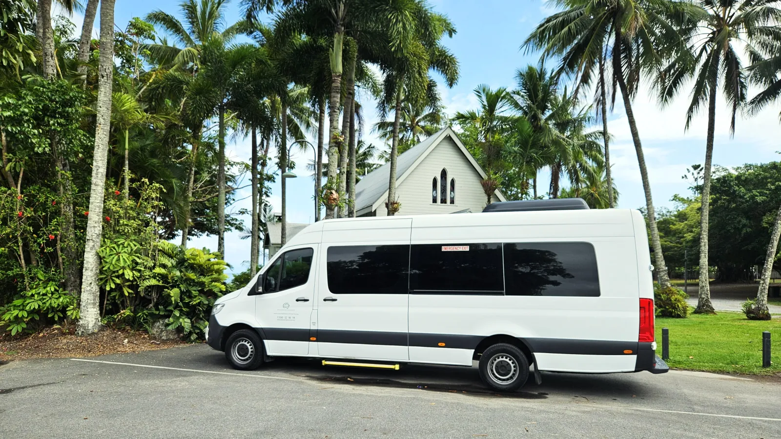 White tour van parked beside palms and a small chapel